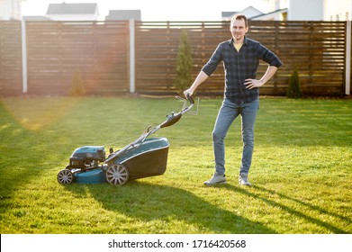 Portrait Of Guy With A Lawn Mower On A Back Yard Of Private House, He Stands And Smiles. Care About Backyard