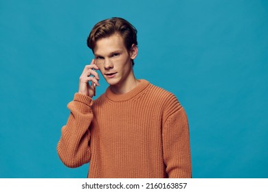 portrait of a guy on a blue background in an orange sweater talking on the phone - Shutterstock ID 2160163857