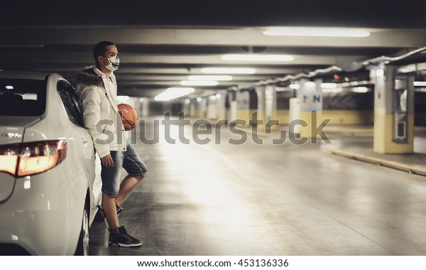 portrait of a guy in the parking lot next to the car\
with a basketball in\
mask