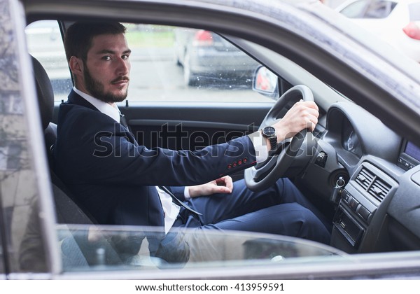 The portrait of the guy in the suit sitting behind\
the wheel of a car