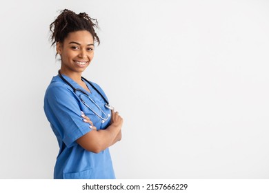 Portrait of half-turned positive female black doctor posing with crossed arms smiling looking at camera isolated on white studio wall, wearing blue coat and stethoscope, mockup, free copy space - Powered by Shutterstock