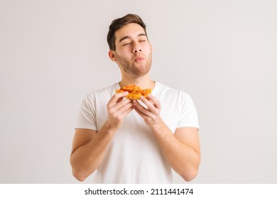 Portrait of handome young man with enjoying eating delicious slice of pizza, with closed eyes from pleasure on white isolated background. Studio shot of hungry male student eating tasty food. - Shutterstock ID 2111441474