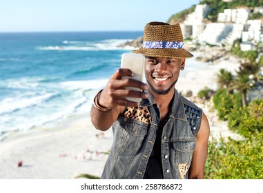 Portrait of a handsome african american man smiling and taking selfie while on vacation at the beach