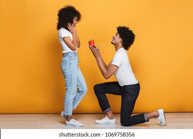 Portrait of a handsome african man proposing to his girlfriend isolated over yellow background