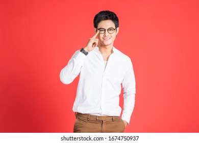 portrait handsome asian businessman adjusting his glasses facial hair smiling looking straight, hands in pocket wearing casual clothing and black earrings, standing and posing red isolated background - Powered by Shutterstock