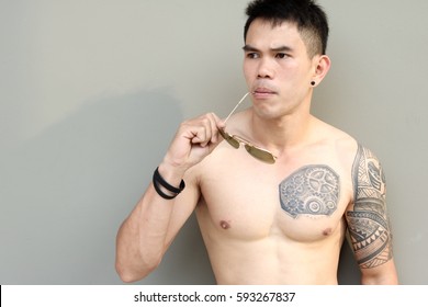 Portrait Handsome Asian Cool Guy. Attractive Man Is Thinking And Missing Someone. Charming Young Man Has Nice Tattoo And Perfect Body. Muscle Man Look Healthy. He Hold And Bite Sunglasses. Copy Space