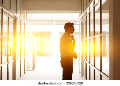 Portrait of handsome Asian Indian businessman grooming using a office mirror to tidy his tie knot, in office building block, beautiful golden sunlight at background.