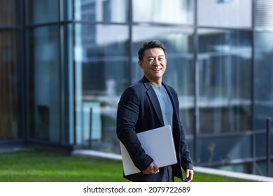 Portrait Handsome Asian Man A University College Teacher, Businessman, Scientist Or Educator. Walks Down The City Street Modern Campus With A Laptop Folder In His Hands. Goes Outside, Outdoor