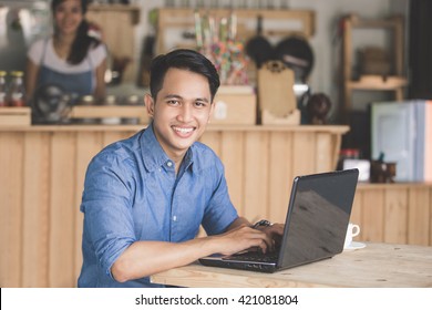 portrait of handsome asian smiling man using laptop in the cafe