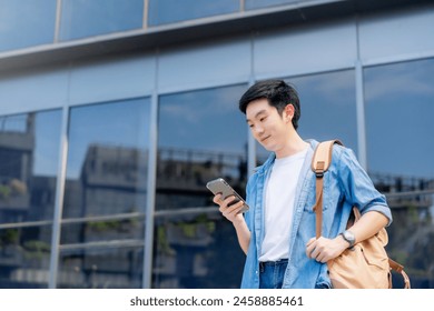 Portrait of handsome Asian student using smartphone. A young man standing outdoor happy smiling with holding mobile phone - Powered by Shutterstock