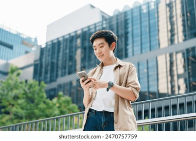 Portrait of handsome Asian student using smartphone. A young man standing outdoor happy smiling with holding mobile phone - Powered by Shutterstock