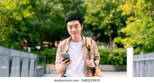 Portrait of handsome Asian student using smartphone. A young man walking outdoor happy smiling with holding mobile phone - Powered by Shutterstock