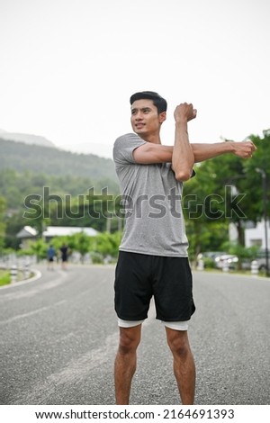Portrait of a handsome asian young in active and comfy sportswear stretching his arms and body before running, training or jogging.