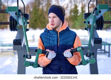 Portrait Of Handsome Athletic Fit Fitness Guy, Young Strong Man Is Training Muscles, Workout Outside In Park Training Outdoors At Gym Machine At Winter Cold Snow Day, Snowy Frosty Weather