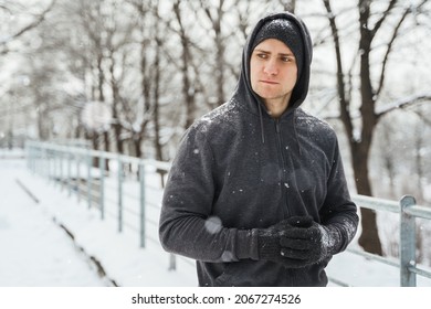 Portrait of handsome athletic man wearing hoodie during his winter workout in snowy city park