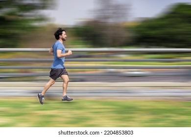 Portrait Of Handsome Attractive Mature Bearded Athletic Latin Man Guy 40s In Casual Blue T-shirt Running At A Park. Speed Concept. Motion Blur Background.