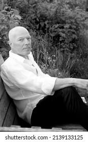 Portrait Of Handsome Bald Man Sitting In Garden. Black And White Photo