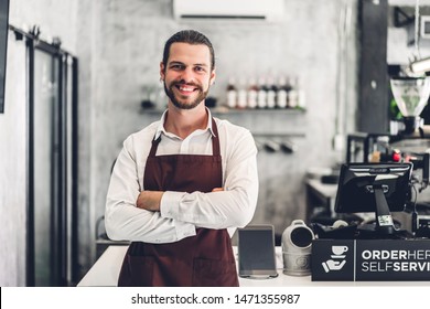 Portrait of handsome bearded barista man small business owner smiling behind the counter bar in a cafe - Powered by Shutterstock