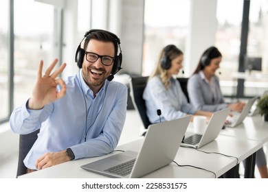 Portrait of handsome bearded business man with headset showing OK sing at call center office