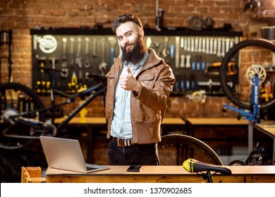 Portrait Of A Handsome Bearded Man As Bicycle Store Owner Or Manager Standing With Laptop At The Bicycle Workshop