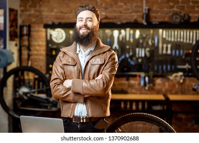 Portrait Of A Handsome Bearded Man As Bicycle Store Owner Or Manager Standing With Laptop At The Bicycle Workshop