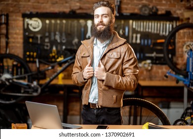 Portrait Of A Handsome Bearded Man As Bicycle Store Owner Or Manager Standing With Laptop At The Bicycle Workshop