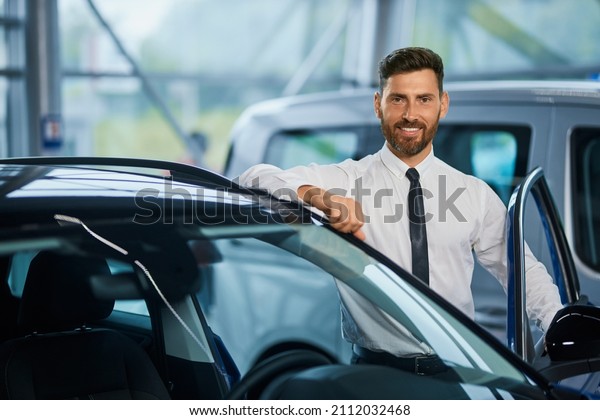Portrait of handsome bearded man in formal clothes\
posing near modern luxury car at showroom. Successful businessman\
buying new vehicle at\
shop.
