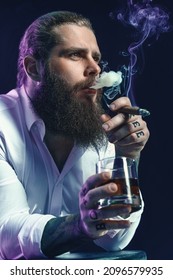 Portrait Of Handsome Bearded Man Smoke A Cigar Holds Glass Of Whiskey, Blows Smoke, Dressed In White Shirt. Studio Shot. 