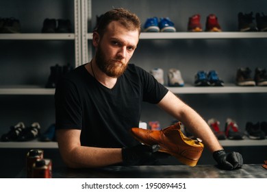 Portrait of handsome bearded shoemaker examining light brown leather shoes during restoration working, looking at camera. Concept of cobbler artisan repairing and restoration work in shoe repair shop. - Powered by Shutterstock