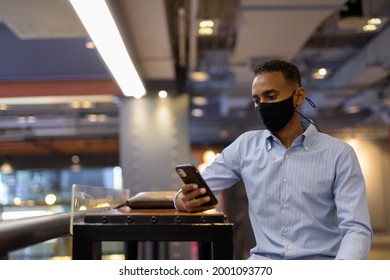 Portrait Of Handsome Black African Businessman Inside Shopping Mall Wearing Face Mask And Using Mobile Phone Horizontal Shot