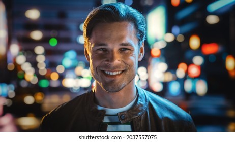 Portrait Of Handsome Blonde Man Smiling, Looking At Camera, Standing In Night City With Bokeh Neon Street Lights In Background. Happy Confident Young Man With Stylish Hair. Close-up Portrait