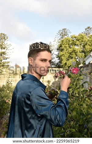 portrait of handsome brunette man wearing fantasy medieval prince costume, romantic silk shirt  royal  golden crown, posing in  castle location  rose garden with dreamy golden  silhouette lighting