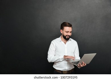 Portrait Of Handsome Brunette Man Working In Office Using Silver Laptop Isolated Over Dark Gray Wall