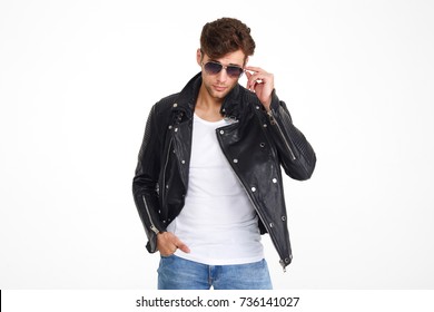 Portrait of a handsome brutal man in a leather jacket and sunglasses posing while standing and looking at camera isolated over white background