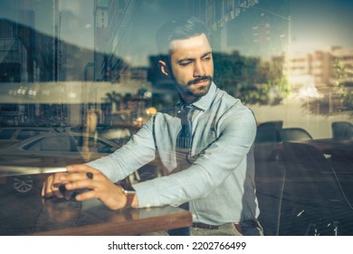 Portrait of handsome business man sitting in a cafe and looking through the window with reflections of urban city. - Powered by Shutterstock