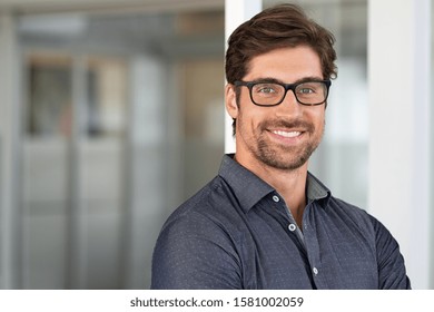 Portrait of handsome businessman standing in modern conference room. Happy young business man looking at camera with copy space. Portrait of successful smiling guy in office wearing eyeglasses.