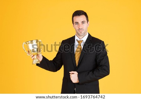Portrait of a handsome businessman wearing white suit and tie while holding a golden trophy with yellow background.
