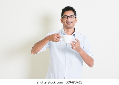 Portrait Of Handsome Casual Business Indian Man Relax And Drinking A Cup Hot Coffee, Standing On Plain Background With Shadow, Copy Space At Side.