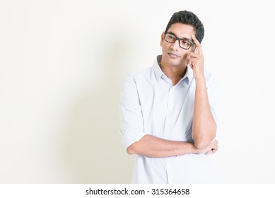 Portrait Of Handsome Casual Business Indian Man Thinking With Serious Face Expression, Standing On Plain Background With Shadow, Copy Space At Side.