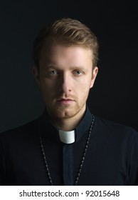 Portrait Of Handsome Catholic Priest Or Pastor With Dog Collar, Black Background.