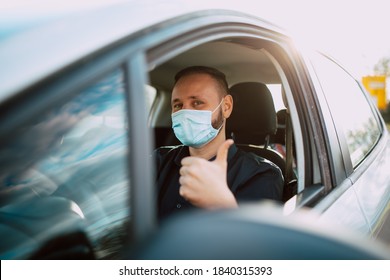 A Portrait Of A Handsome Caucasian Businessman In A Black Shirt With A Face Mask Giving A Thumbs Up While Driving A Car On The Way To Work. Protection During The COVID - 19 Coronavirus Pandemic