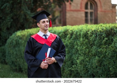 Portrait Of Handsome Caucasian Male Graduate In Graduation Robe Looking At Campus.