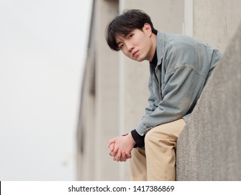 Portrait Of A Handsome Chinese Young Man Sitting And Looking At Camera With Blank Expression, Has Nothing To Do Just Waiting.