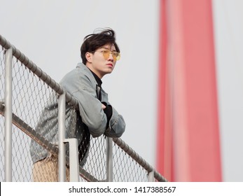 Portrait Of A Handsome Chinese Young Man Standing On Bridge And Looking Away In Wind, Has Nothing To Do Just Waiting.