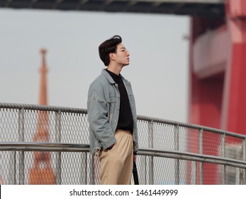 Portrait of a handsome Chinese young man standing and looking away  with hand in pocket in windy sunny day, has nothing to do just waiting.
