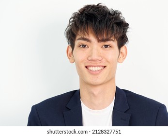 Portrait Of Handsome Chinese Young Man In Dark Blue Leisure Suit Standing And Posing Against White Wall Background. Smiling And Looking At Camera Confidently, Front View.