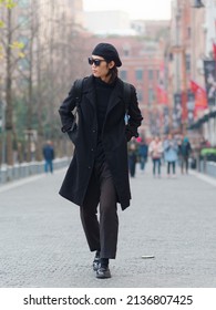 Portrait of handsome Chinese young man wearing black overcoat, sweater and trousers with sunglasses walking on Shanghai street, front view, male fashion, cool Asian young man lifestyle.