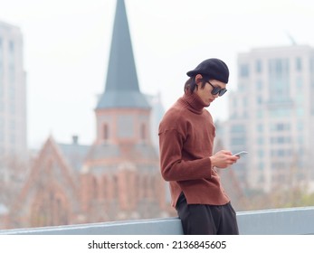 Portrait Of Handsome Chinese Young Man With Sunglasses Standing And Typing At Mobile Phone With Shanghai City Landmarks Background, Male Fashion, Cool Asian Young Man Lifestyle.