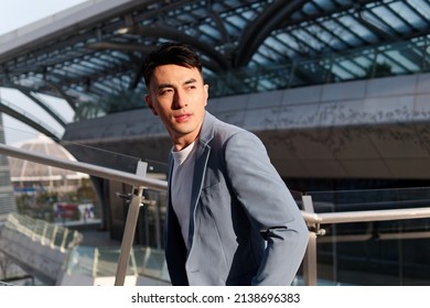 Portrait Of Handsome Chinese Young Man In Light Blue Suit And White Undershirt Walking And Looking Away With Modern City Buildings Background In Sunny Day, Side View Of Confident Businessman.