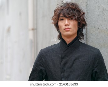 Portrait of handsome Chinese young man in black looking at camera with gray wall background, front view of confident young man.